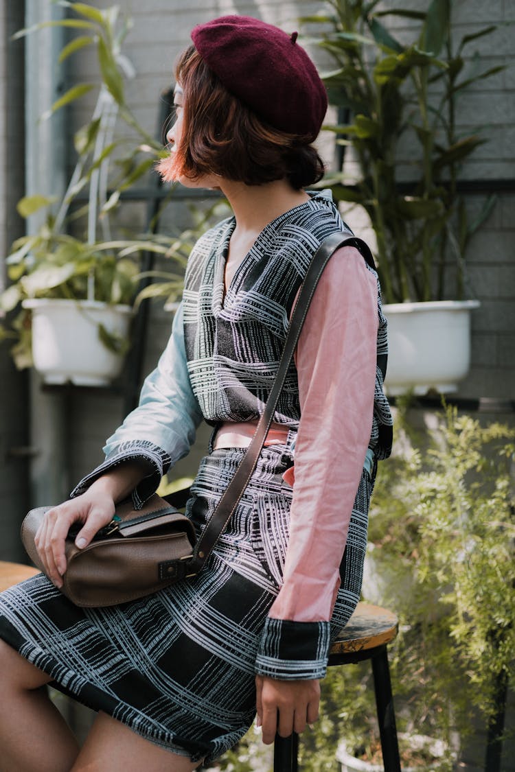 Unrecognizable Asian Woman In Stylish Outfit On Stool In Garden