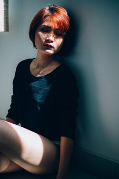 室内，一位红发年轻女子坐在阳光下，若有所思