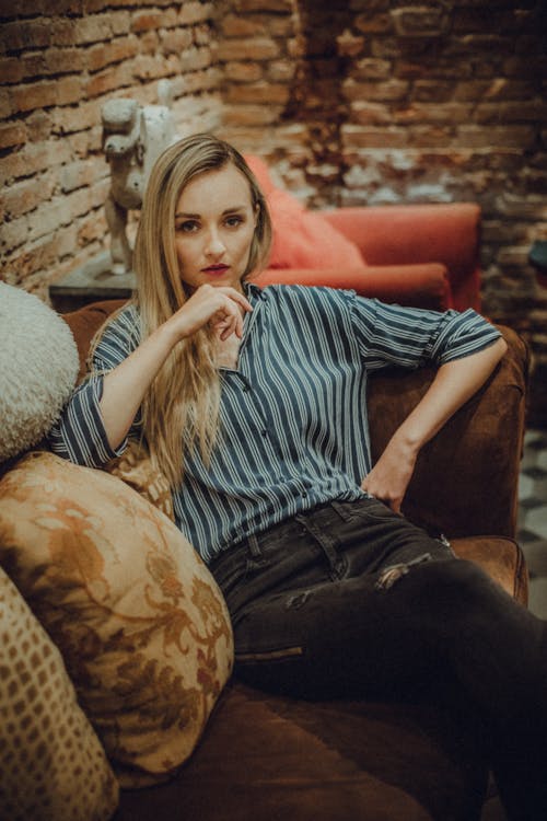 Pensive woman touching chin while sitting on comfy couch in room in loft style