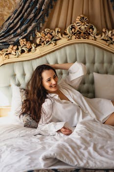 Woman in white shirt smiling while relaxing on an elegant bed with ornate headboard.