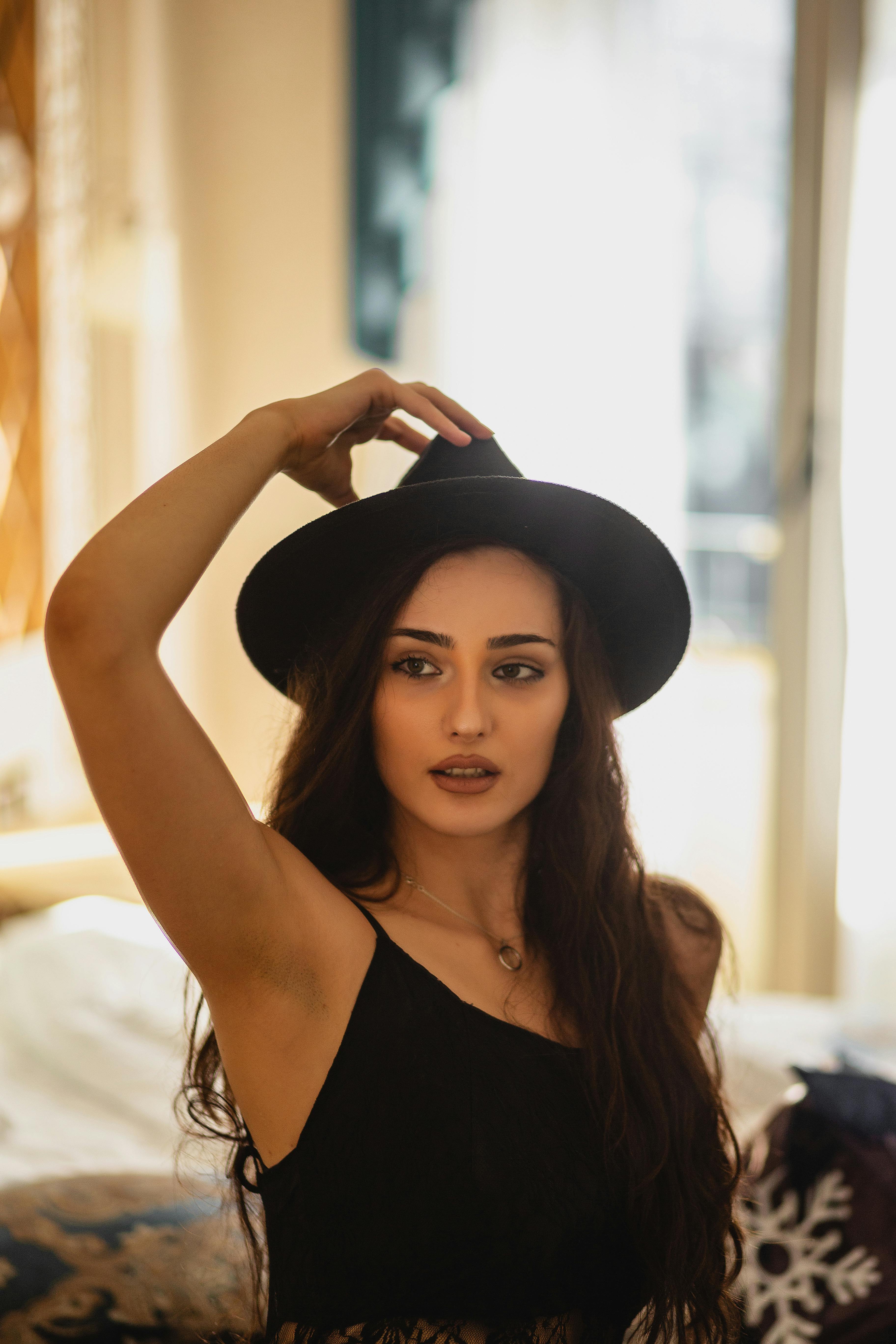 A woman wearing a hat poses elegantly indoors, showcasing fashion and style.