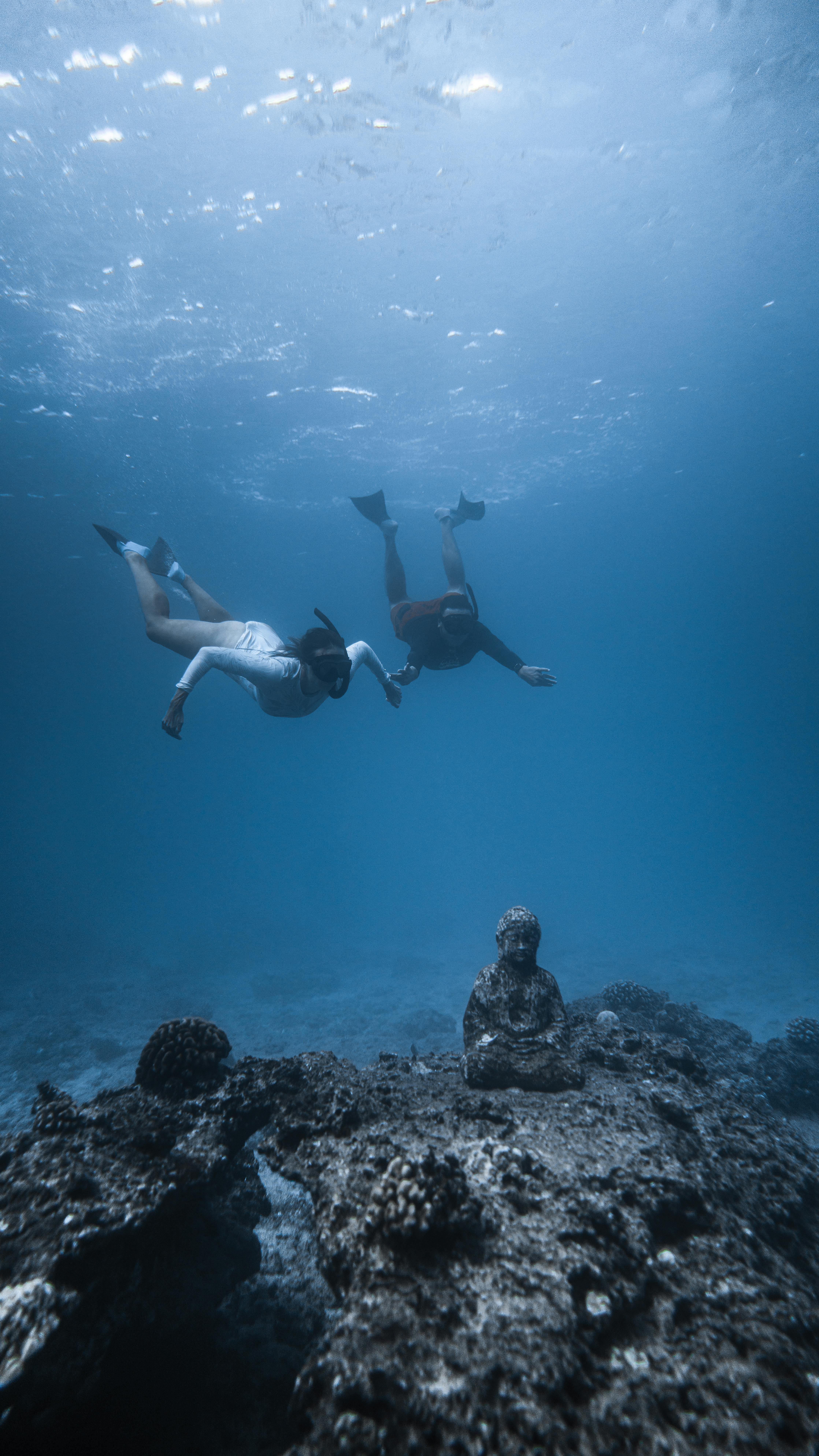 anonymous travelers diving and sightseeing underwater aged buddha statue