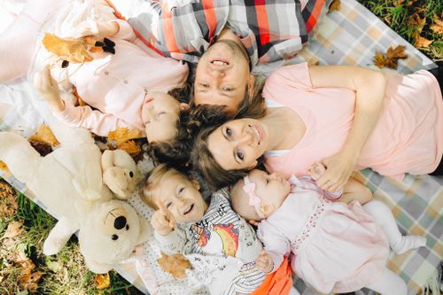 Free A joyful family lying on a picnic blanket outdoors, surrounded by autumn leaves and teddy bears. Stock Photo