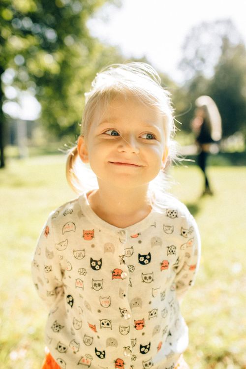 Free A cute young girl in a cat-themed sweater, smiling brightly in an outdoor park. Stock Photo