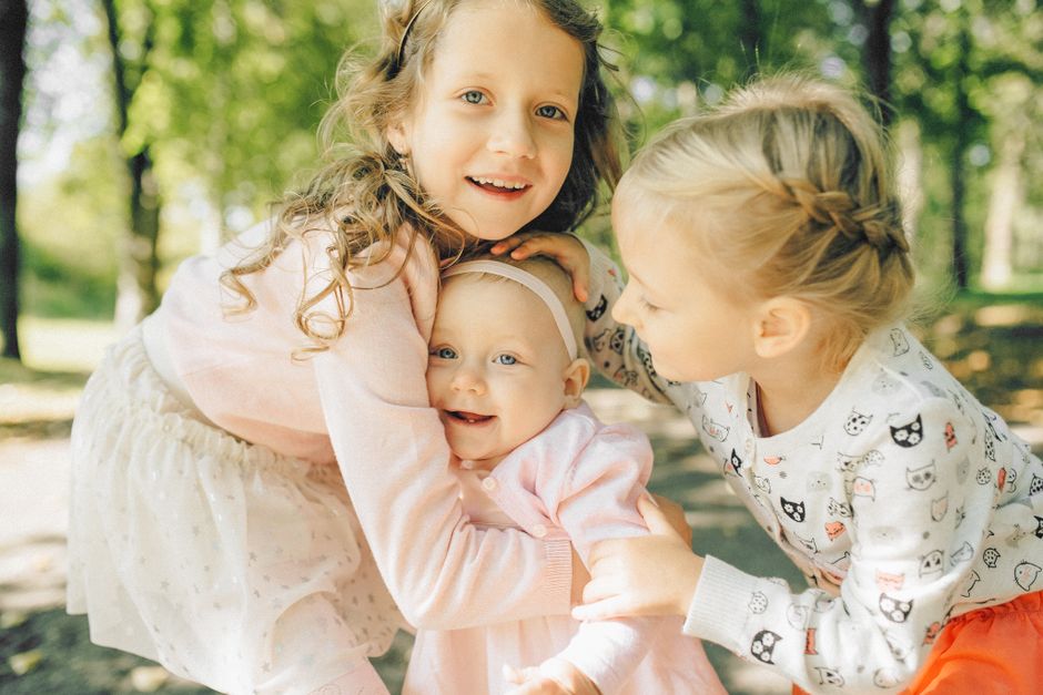 Three joyful siblings hugging in a sunlit park, capturing the essence of childhood and family closeness.