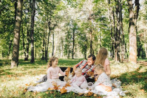 Free A joyful family picnic with parents and children surrounded by green trees and sunshine. Stock Photo