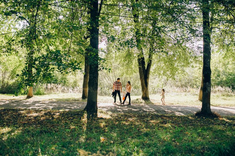 A family enjoying a sunny day walking through a green park in summer.