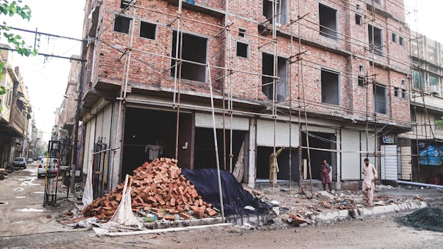 A multi-story building under construction with exposed brick and scaffolding, debris on the ground.