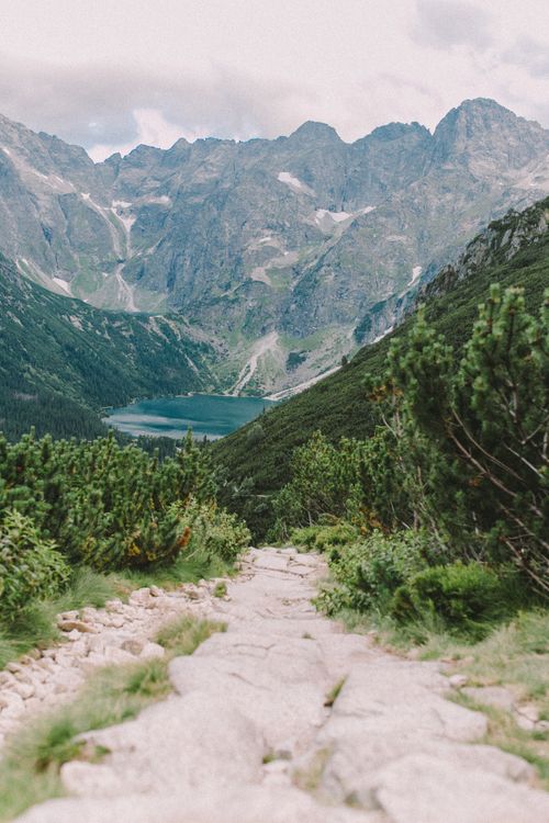 Free Explore a stunning mountain pathway descending to a tranquil lake with majestic peaks in the backdrop. Stock Photo