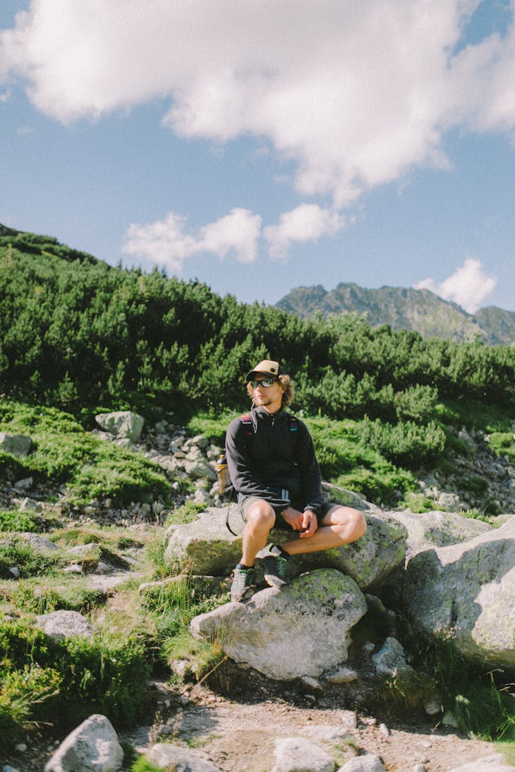 A Man In Black Long Sleeves Sitting On The Rock Near The Green Trees