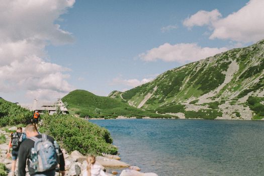 Hikers enjoy a scenic walk by a tranquil mountain lake under a clear blue sky.