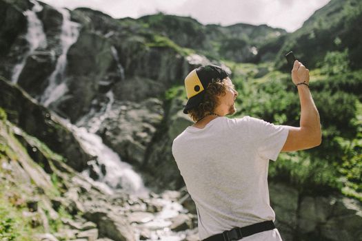 一名年轻人在徒步旅行时，于阳光明媚中拍下了山峰瀑布的壮丽景色