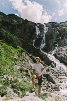 夏季徒步旅行时，一位冒险家在岩石山腰的雄伟瀑布旁摆姿势
