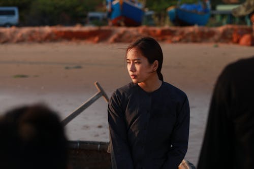 Young melancholic ethnic female in black wear looking away in boat on river in evening