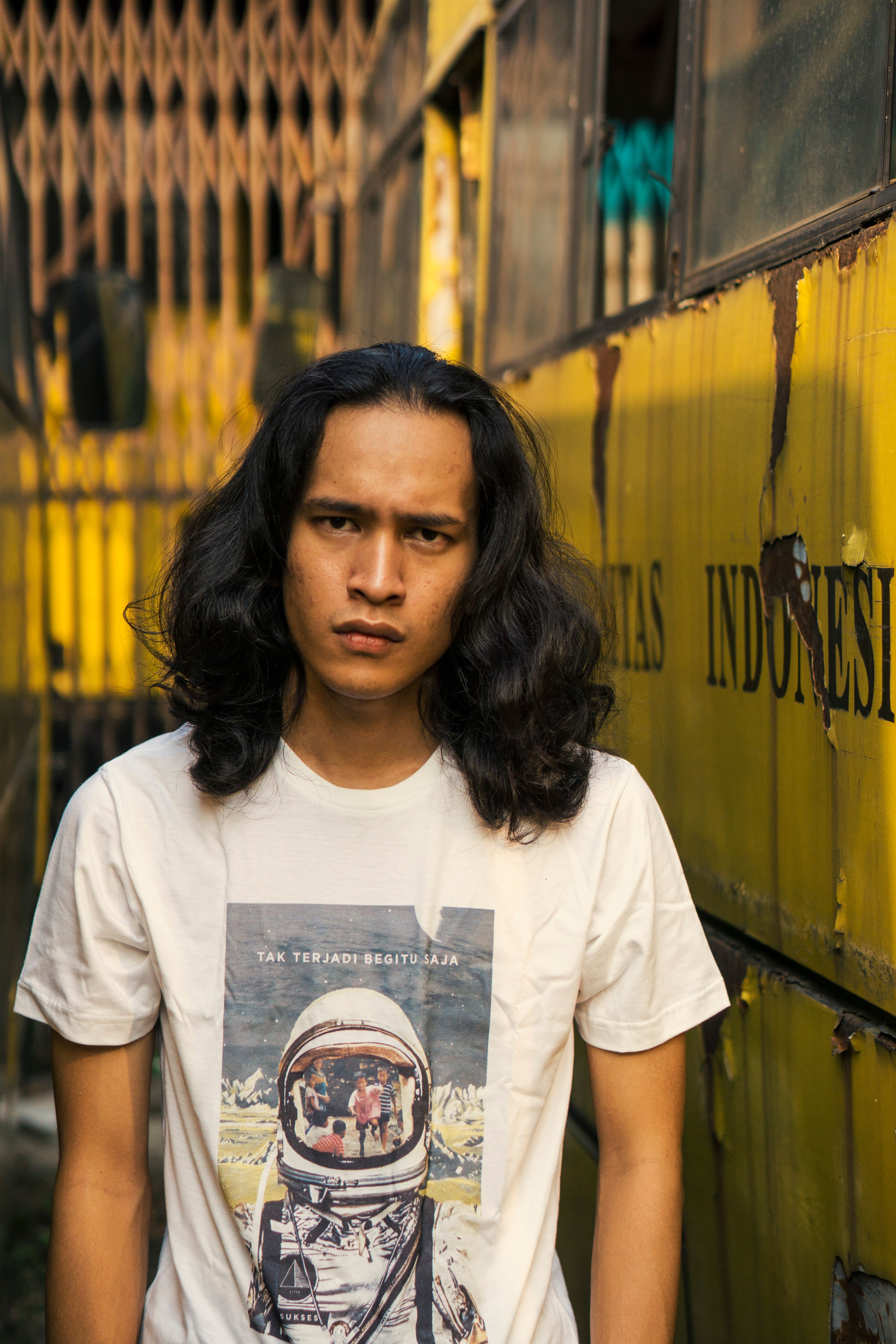 Portrait of a young man with long hair standing next to a vintage bus.