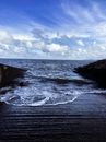 Vibrant blue sky covered with clouds above dark wavy endless ocean and slope on coast
