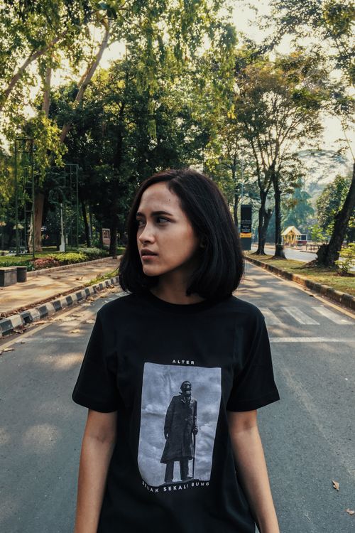 Free Portrait of a young woman in a black shirt standing on a street in Indonesia surrounded by trees. Stock Photo