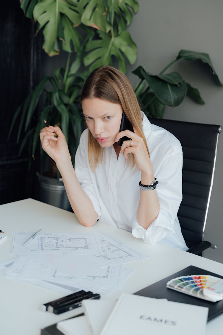 A Woman In White Top Sitting On The Chair While Talking On The Phone