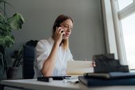 一名女子在室内办公桌前一边查看文件一边打电话