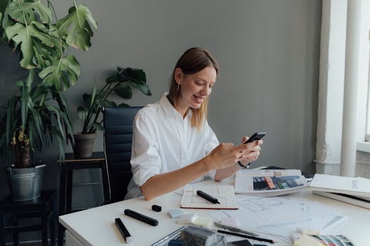 一名女性专业人士在办公桌前工作，用智能手机查看建筑平面图