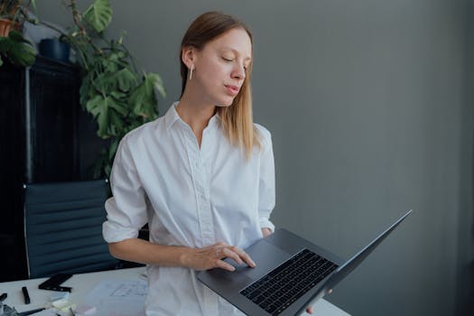 Woman using laptop in a modern office setting, embodying professional remote work lifestyle.