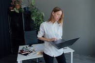 Woman in White Dress Shirt and Black Pants Holding Macbook