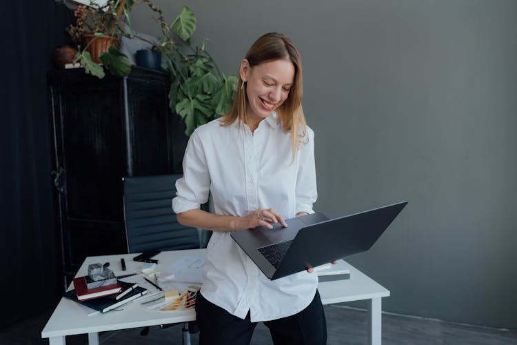 Smiling Woman Using A MacBook While Leaning On A Desk