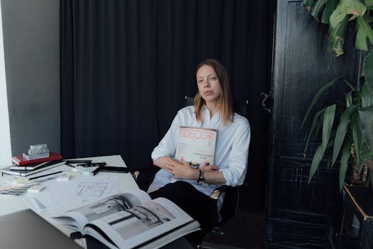 A female interior designer holding a design magazine in her modern home office workspace.