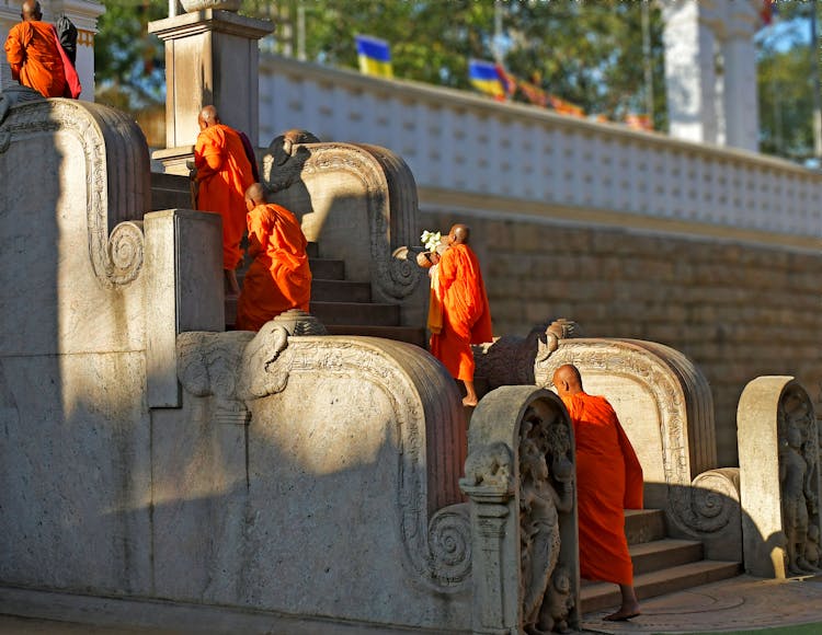 Monks In Vibrant Orange Clothes Waking On Carved Stone Steps