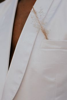 Crop African American person in white elegant formal jacket with small fragile beige ear of plant in front pocket