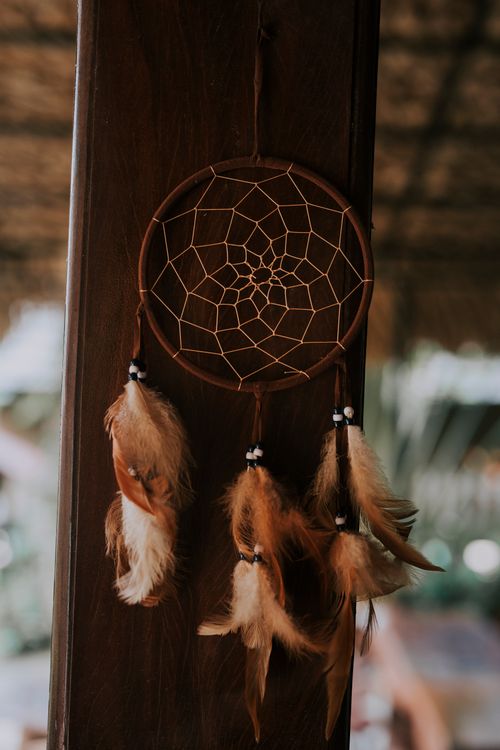 Free Close-up of a dreamcatcher with feathers hanging against a wooden background, capturing a rustic aesthetic. Stock Photo