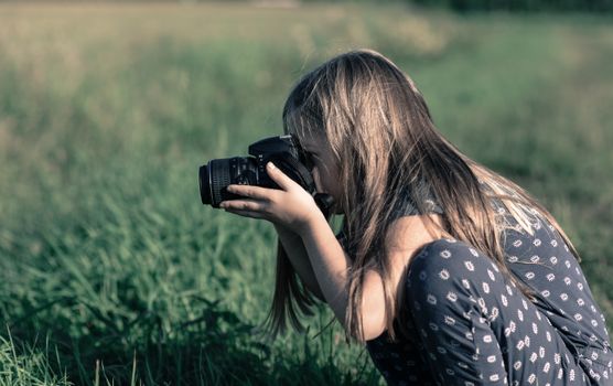A young girl taking photos in a grassy field, showcasing nature photography.