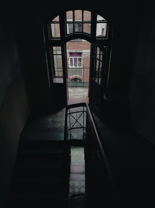 From above of staircase with railings inside multistory residential house with window and metal fence located near building on street