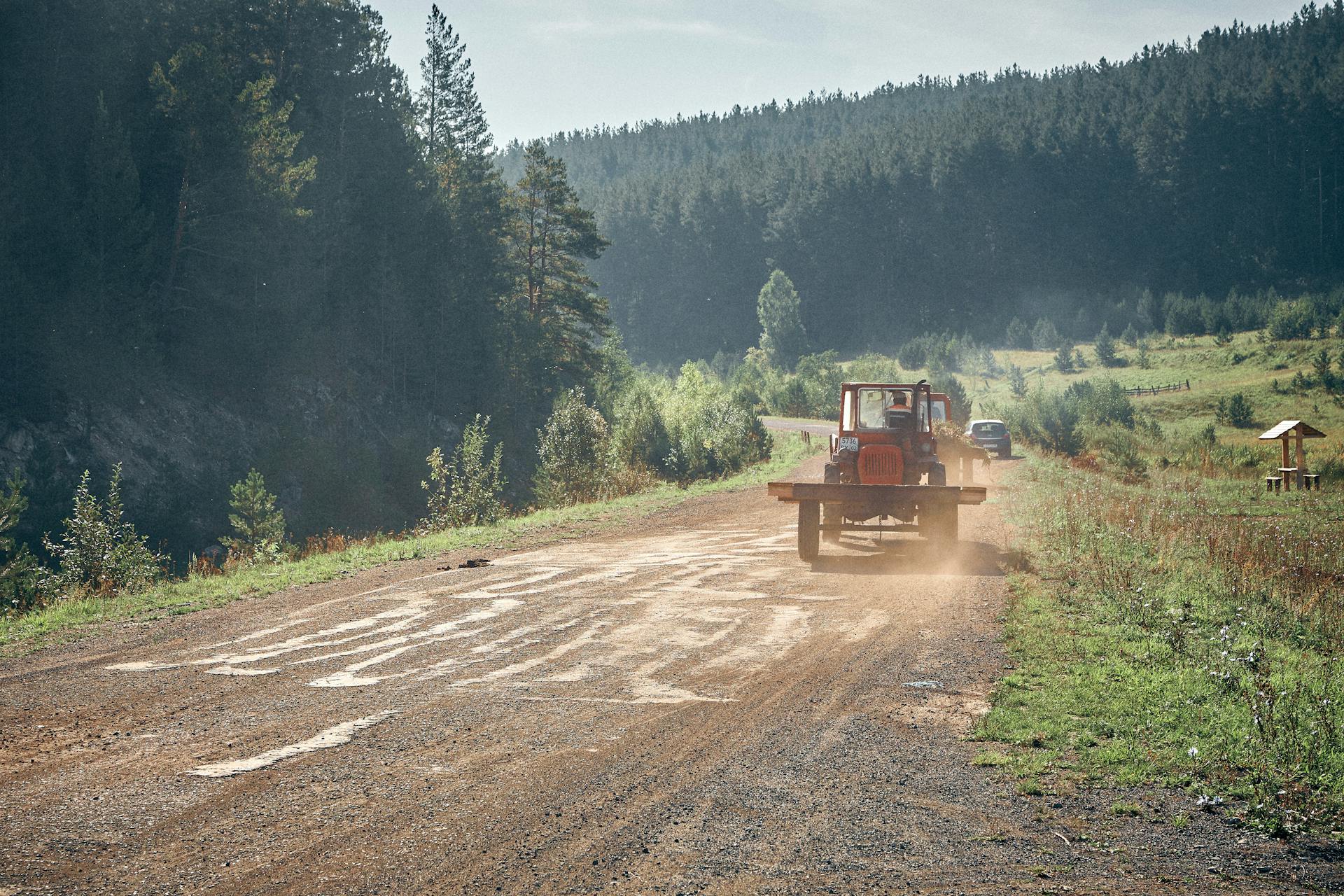 A scenic rural scene with a tractor traveling on a forest road surrounded by lush greenery.