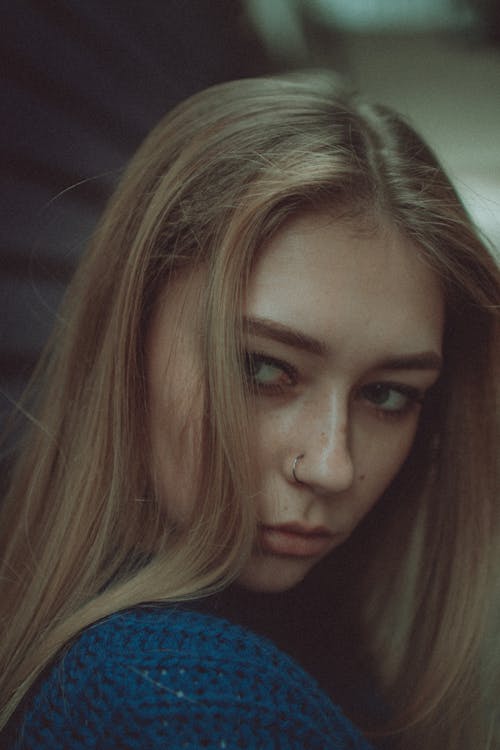 Side view thoughtful young female with nose piercing standing on blurred background and looking away attentively