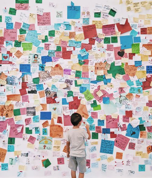Free A child stands before a wall covered with colorful notes and messages, exploring creativity and expression. Stock Photo