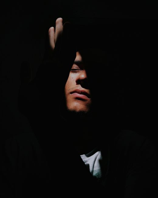 Dramatic portrait of a man with eyes closed, obscured by shadows, evoking introspection.