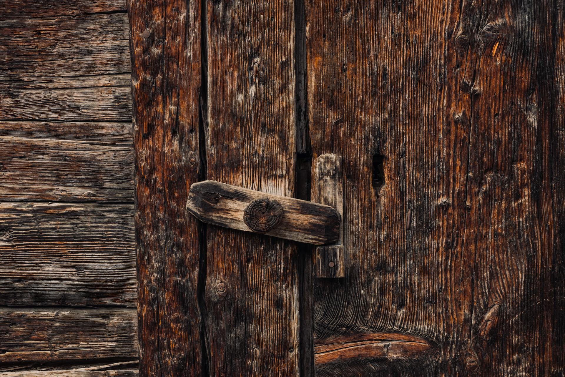 Close-up of a rustic, weathered wooden door with an old-fashioned lock in a rural setting.