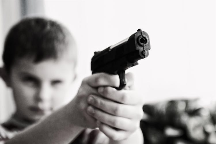 Grayscale Photo Of A Boy Aiming Toy Gun Selective Focus Photography