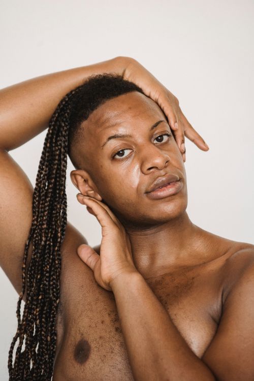 Free Confident African American male with naked torso and hand on tilted head with Afro braids looking at camera and standing on white background with hand near face Stock Photo