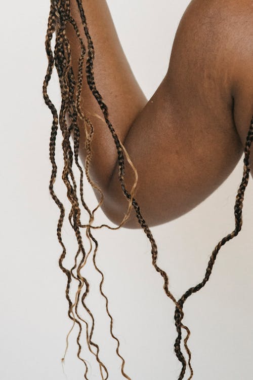 Unrecognizable African American person detangling long Afro braids while standing on white background in light studio