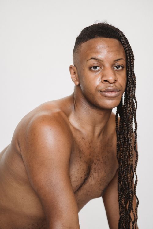 Free Confident African American male with naked torso leaning forward and looking at camera while sitting on white background in studio Stock Photo