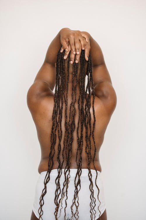 Black androgynous man with Afro braids touching head in studio