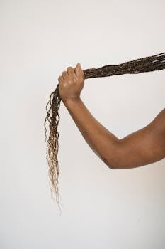 An arm holding a long braid against a plain white backdrop, showcasing hairstyle details.