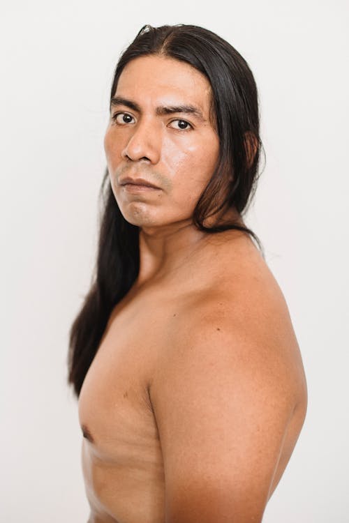 Shirtless ethnic man with long hair standing in light studio