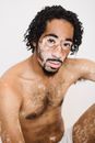 Young unshaven African American male with patchy skin sitting with naked torso and looking at camera on white background