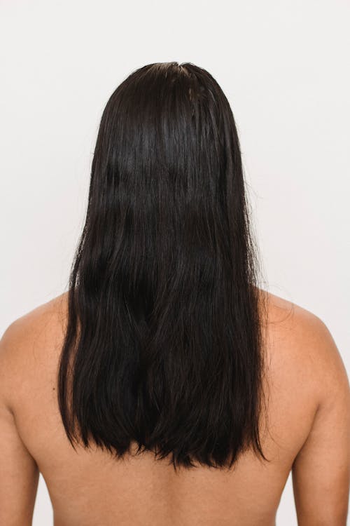 Back view of anonymous ethnic person with naked torso and black hair on white background