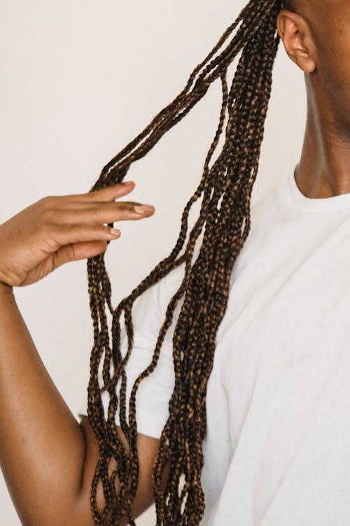 Crop anonymous black man with long braids touching hair