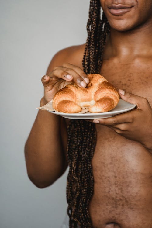 Free Crop shirtless black man with long hair eating croissant Stock Photo