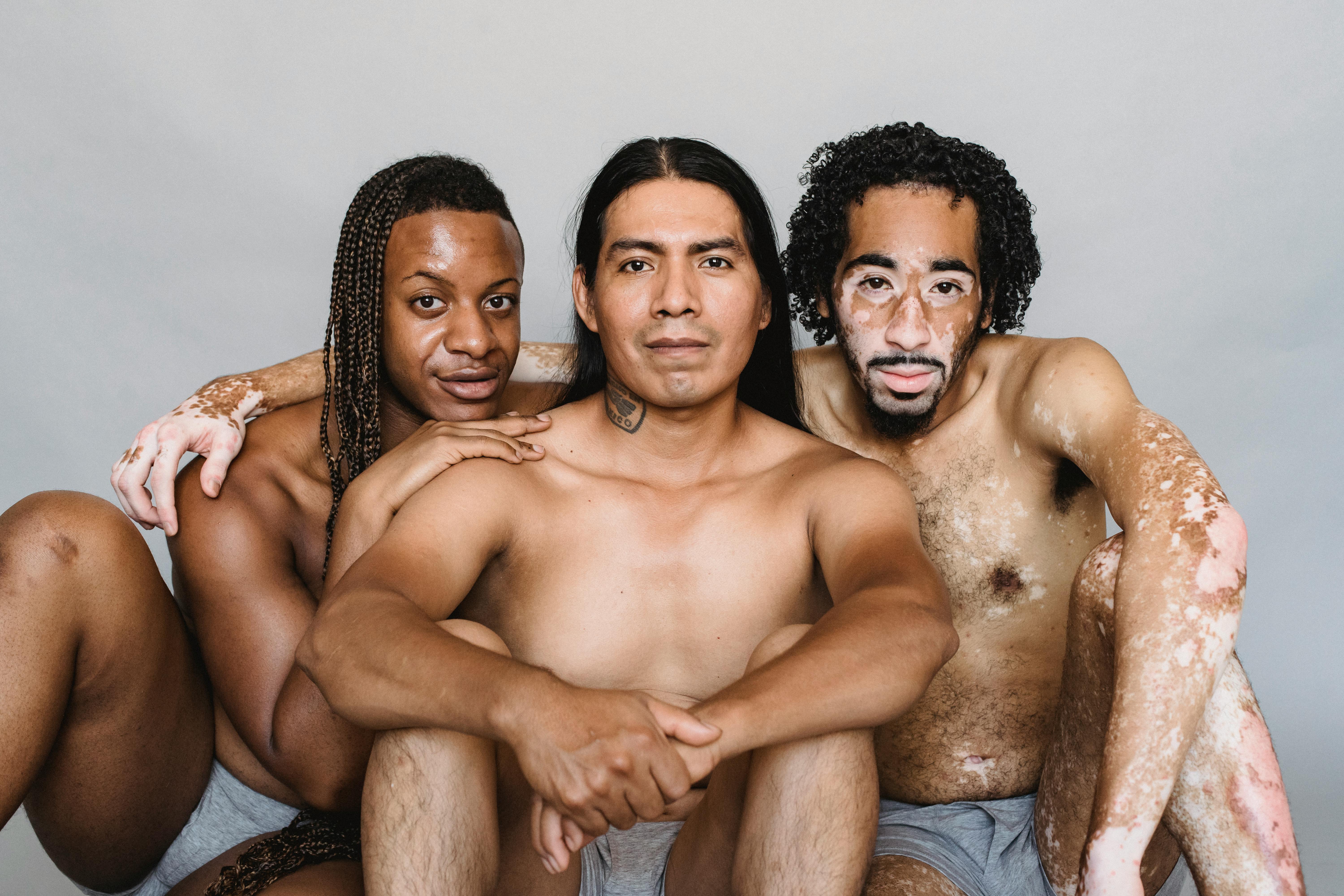 positive shirtless multiethnic men sitting on floor and embracing